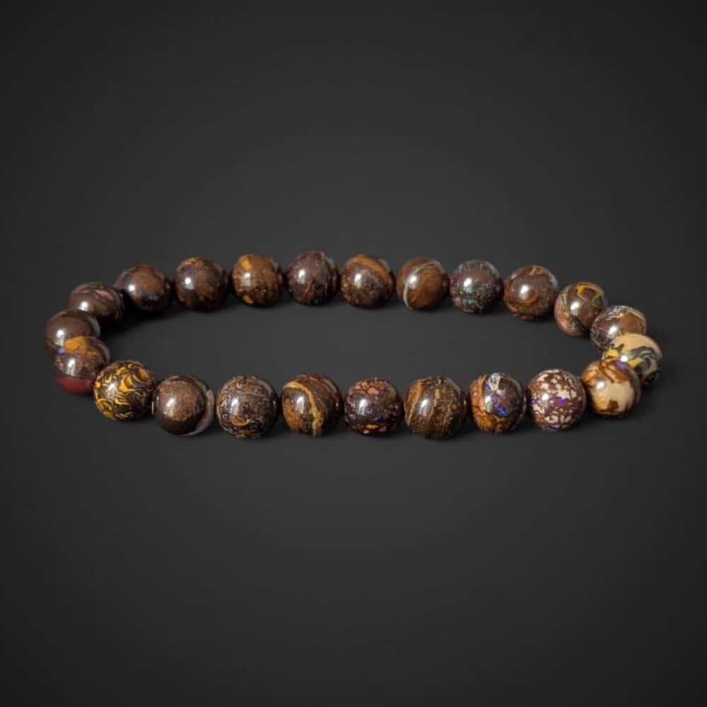 Bracelet en opale Boulder naturelle 8 mm présenté sur fond noir, mettant en valeur les reflets exceptionnels et la qualité premium de chaque perle.