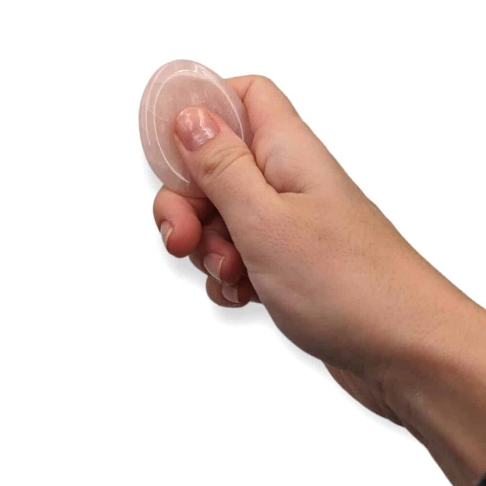 Main utilisant un worry stone en quartz rose en frottant la pierre avec le pouce